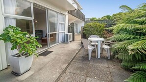 A patio with a white table and chairs, a potted plant, and a sliding glass door leading to a room. - Rotorua Central Accommodation  (Rotorua)