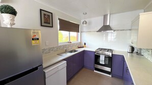 A modern kitchen with a stainless steel refrigerator, a dishwasher, a gas stove, and a window providing natural light. - Rotorua Central Accommodation  (Rotorua)