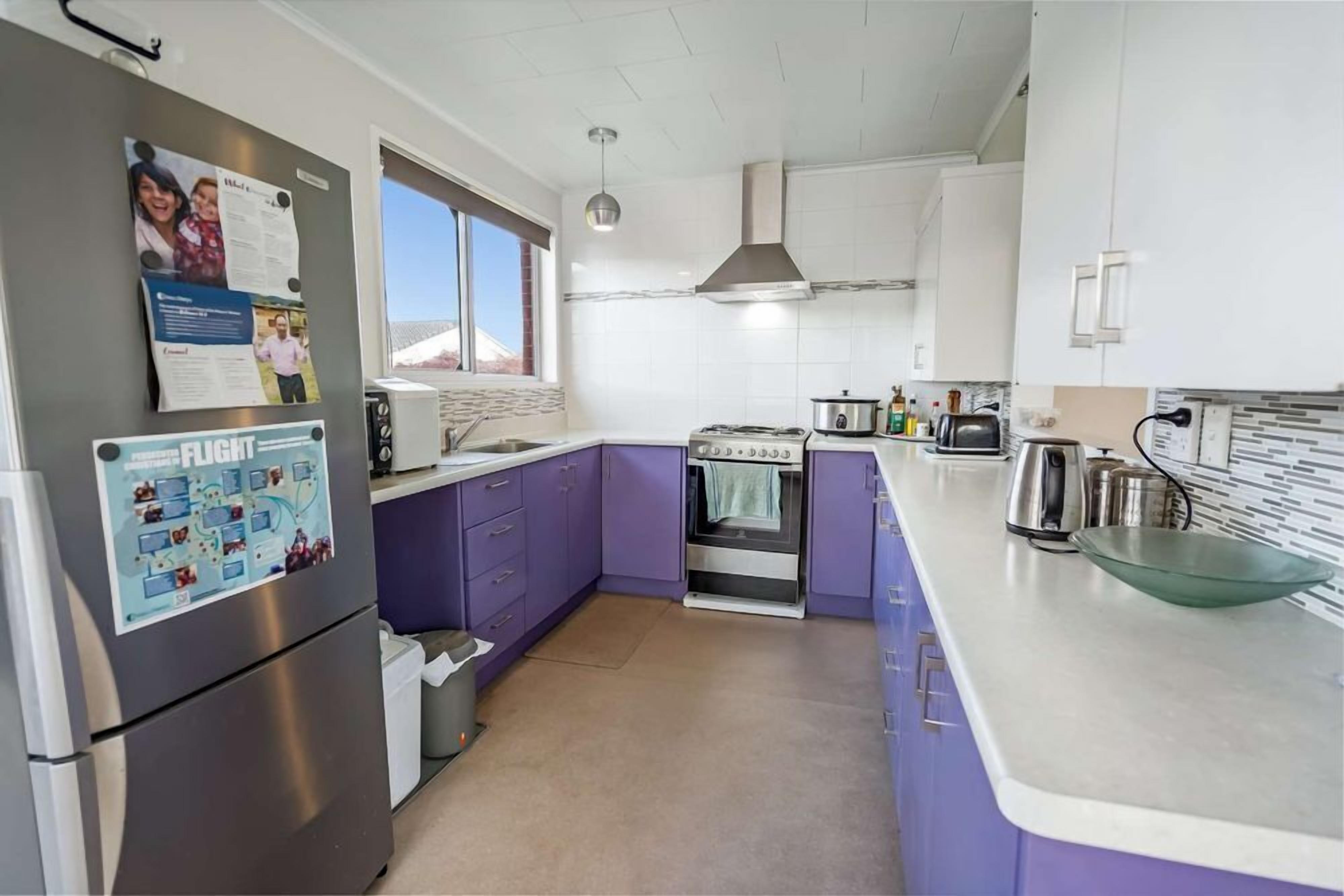 A kitchen with purple cabinets, a stainless steel refrigerator, a stove, and a window providing natural light.
