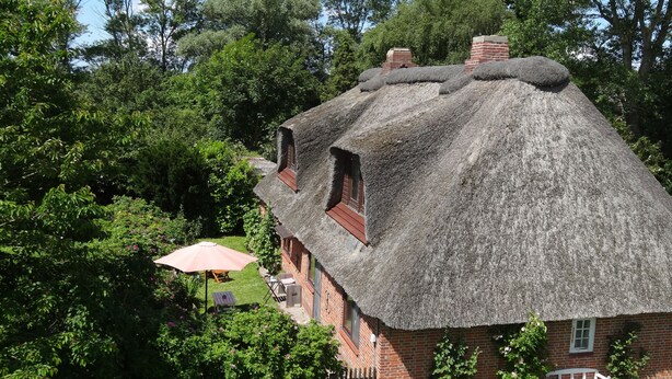 A traditional thatched-roof house with a brick exterior, a wooden bench, and a small garden area with a fence. - Idyllic thatched house directly on the Eider dike for 2 to 10 people (Oldenswort)