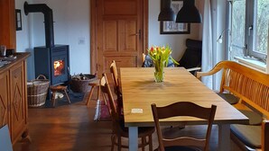 A cozy dining area with a wooden table, chairs, a bench, a fireplace, and a window with a view. - Idyllic thatched house directly on the Eider dike for 2 to 10 people (Oldenswort)