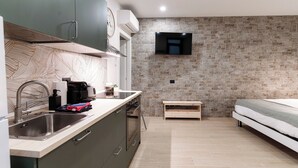 A modern kitchen with a built-in stove, sink, and a flat-screen TV mounted on a stone wall. - Victoria Studio 1  (Como)