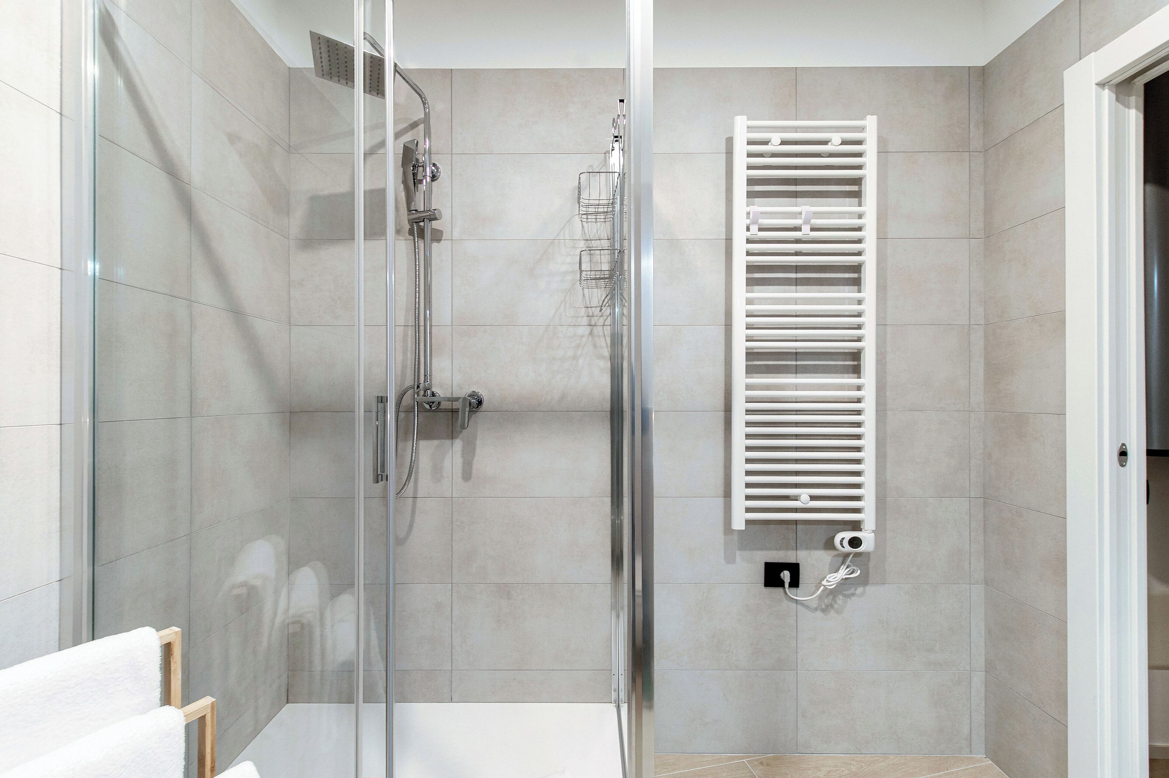 Une salle de bain moderne dotée d’une douche à parois de verre, d’un porte-serviettes blanc et d’un radiateur encastré.