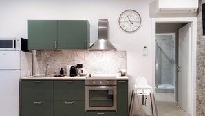 A modern kitchen with a built-in oven, a microwave, and a sink. There is a clock on the wall and a baby high chair near the entrance. - Victoria Studio 1  (Como)