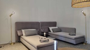 Ett modernt sovrum med en grå bäddsoffa, ett litet sängbord med en lampa och en golvlampa.