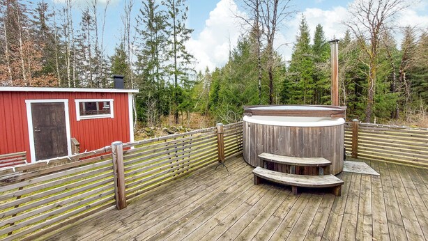 A wooden deck with a hot tub, a red building, and a wooden fence.