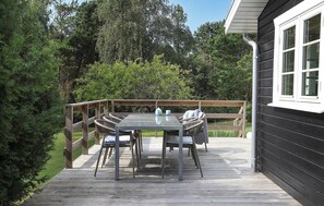 Une terrasse en bois avec une table et des chaises, entourée de verdure.