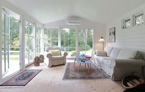 Una habitación amplia con un gran ventanal, techo blanco, sofá color beige, sillón blanco, una mesita y una lámpara de pie.