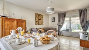 A dining area with a table set for breakfast, a wooden cabinet, and a view of the outdoors through a glass door. - Awesome home in Rochefort (Rochefort)