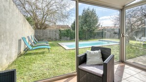 A sunlit room with a glass door leading to a backyard with a swimming pool, a grassy lawn, and a wooden fence. - Awesome home in Rochefort (Rochefort)