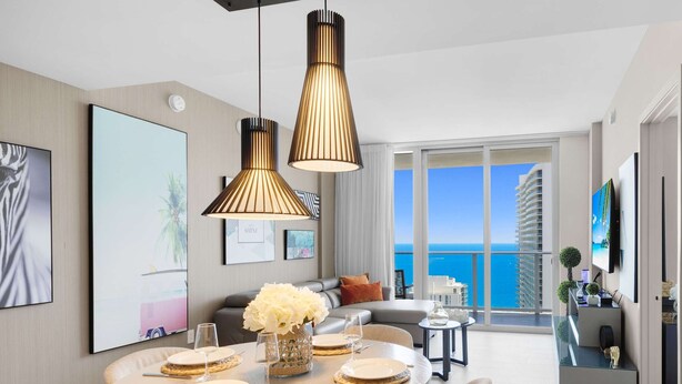 A modern living room with a dining area, large windows with a view of the sea, and contemporary furnishings. - 2Br - Bay View -Apt w/ Amenities (Hollywood)