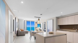A modern kitchen with a central island, a dining area with a view of the sea, and a living area with a sofa and a large window. - 2Br - Bay View -Apt w/ Amenities (Hollywood)