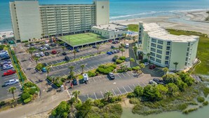 A hotel with a large parking lot, a sports field, and a view of the beach. - Oceanfront Resort 2Br Condo Pools and Hot Tubs (Myrtle Beach)