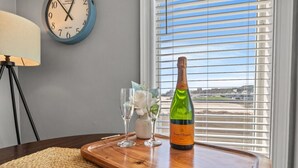 A wooden tray with a bottle of wine, glasses, and a decorative item on a table by a window with blinds. - Oceanfront Resort 2Br Condo Pools and Hot Tubs (Myrtle Beach)