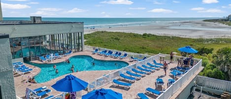 A rooftop pool area with multiple swimming pools, sun loungers, and umbrellas.
