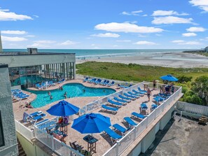A rooftop pool area with multiple swimming pools, sun loungers, and umbrellas.