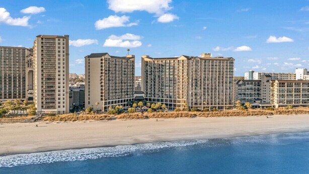 A coastal hotel with multiple high-rise buildings, a sandy beach, and a clear blue sky.