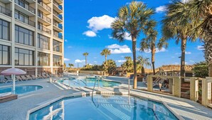 A hotel pool area with multiple pools, lounge chairs, and palm trees.