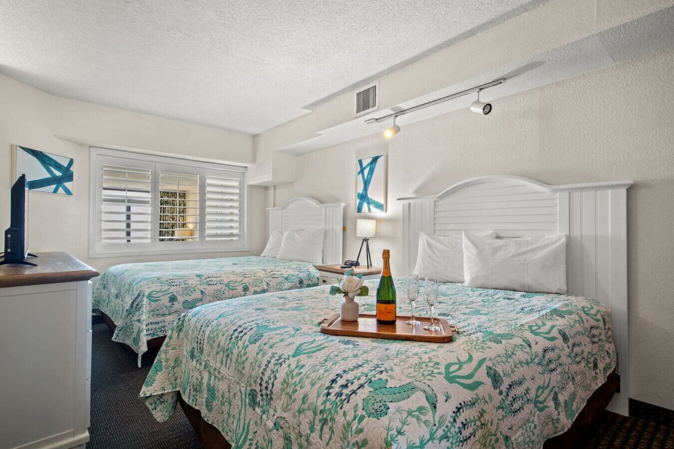 Une chambre d’hôtel avec deux lits, un bureau et une fenêtre avec des stores.