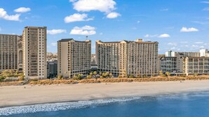 Un hotel costero con varios edificios altos, una playa de arena y un cielo azul despejado.