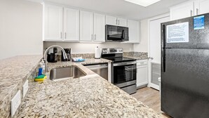 Una cocina moderna con armarios blancos, encimera de granito, refrigerador negro, microondas, horno y lavavajillas.