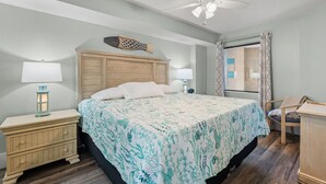 Un dormitorio con cama, mesitas de noche, un escritorio, ventilador de techo y ventana con cortinas.