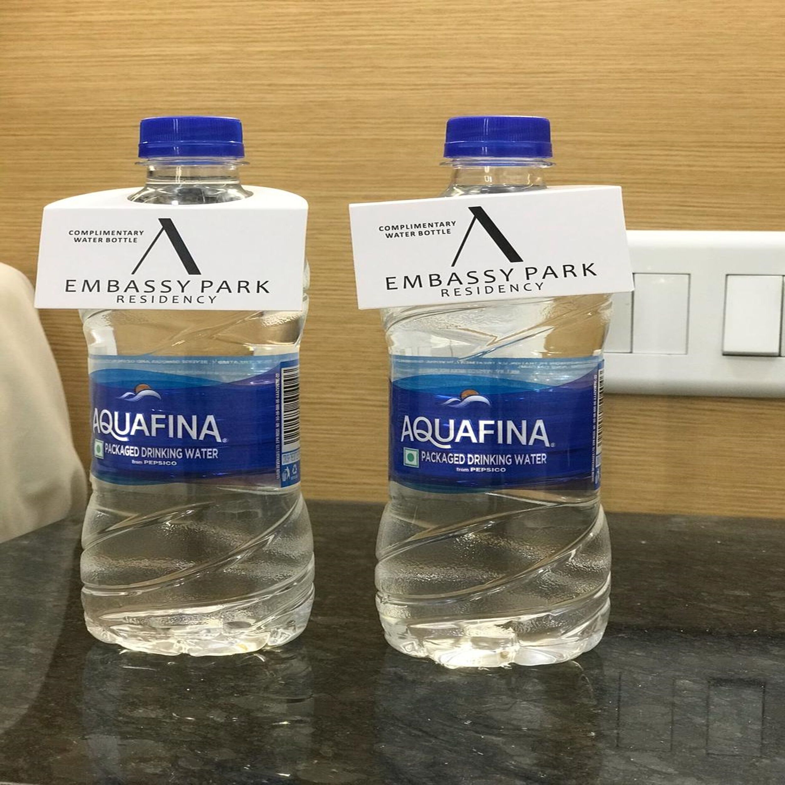 Two Aquafina water bottles on a countertop with labels indicating they are complimentary for Embassy Park Residency.