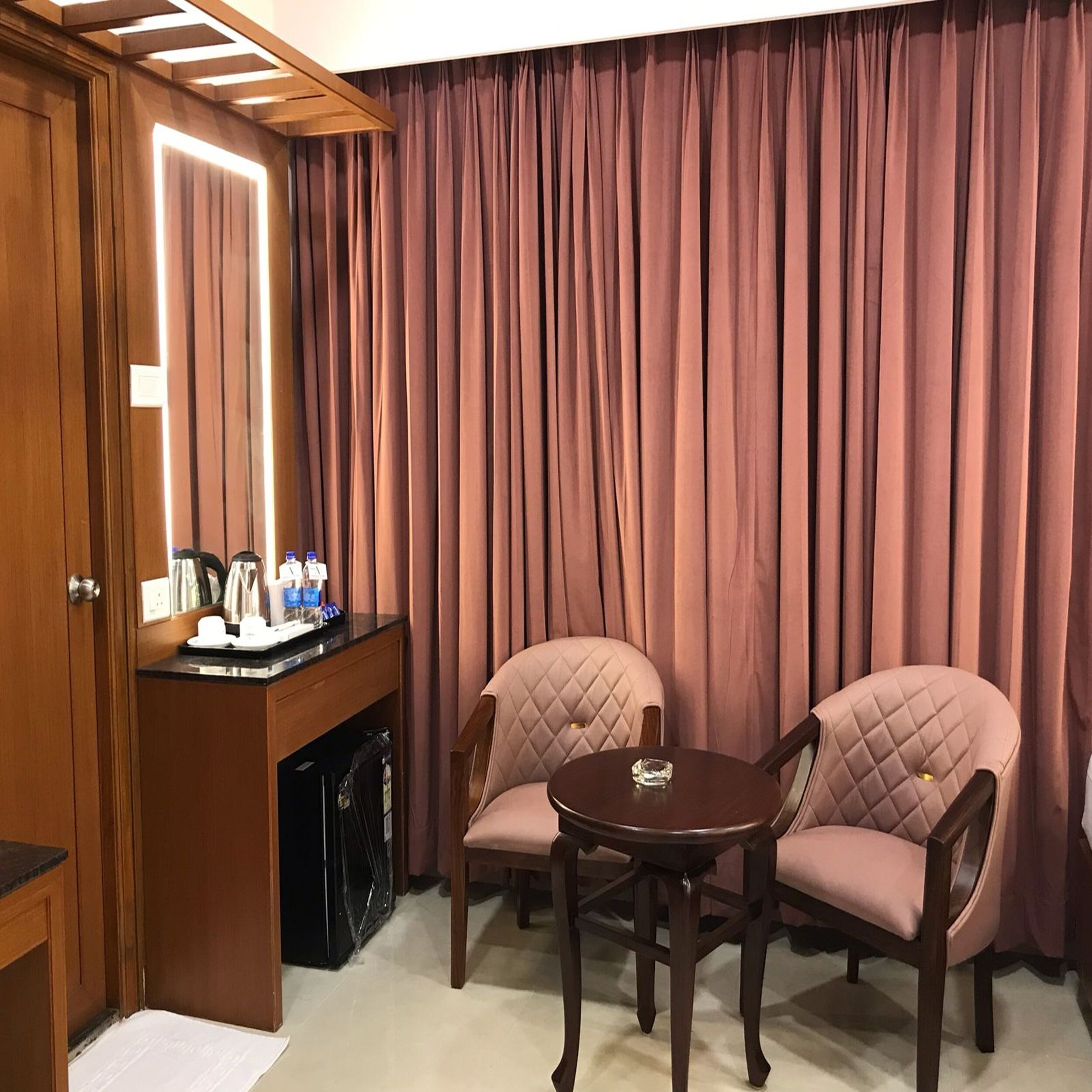Habitación de hotel con un escritorio de madera, dos sillones acolchados, una mesa redonda y un gran telón de fondo.