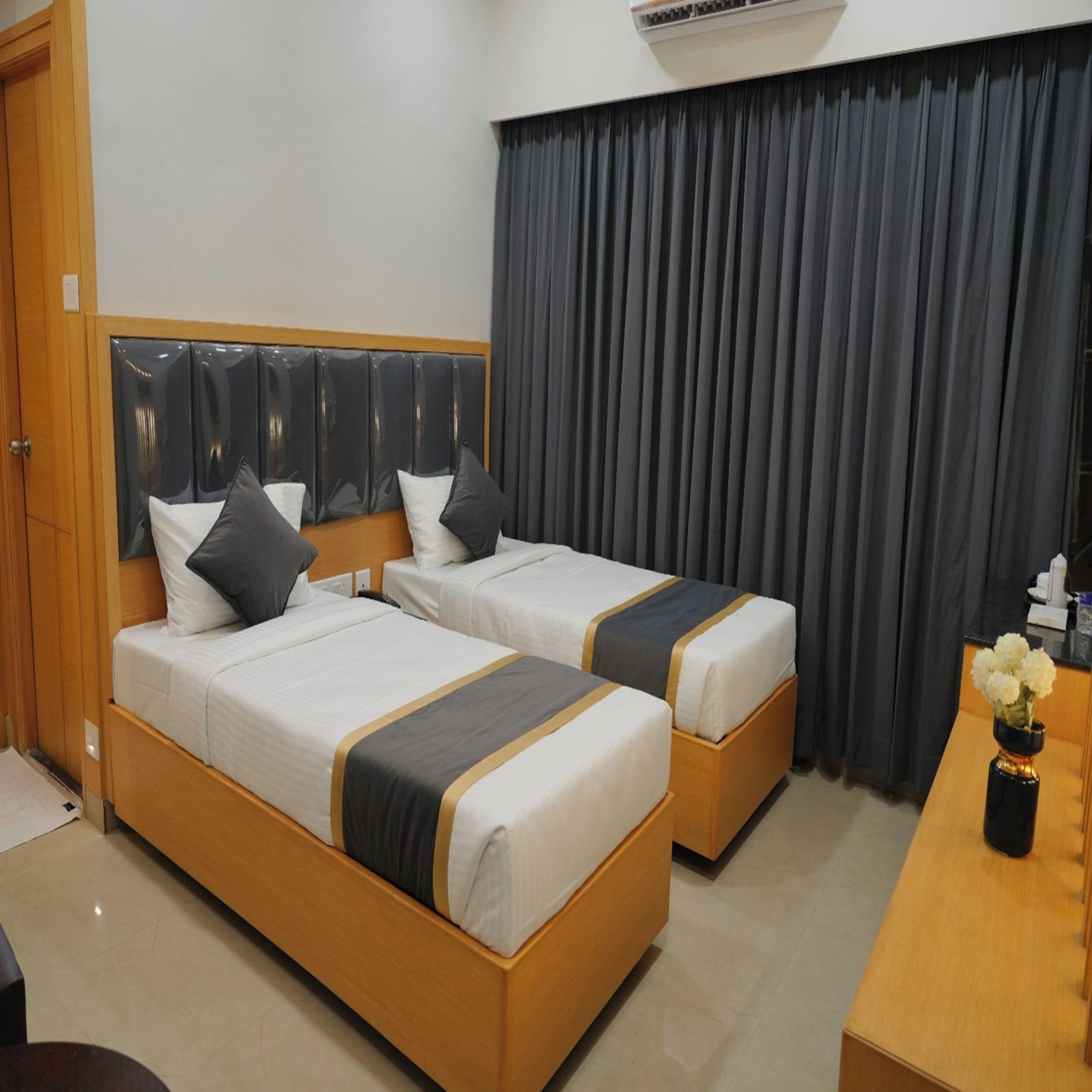 A hotel room with two beds, a wooden headboard, a desk, and a curtain.