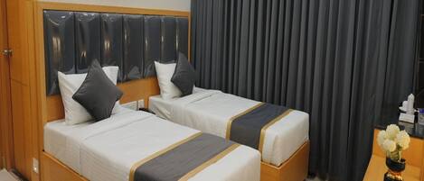 Una habitación de hotel con dos camas, un cabecero de madera, un escritorio y una cortina.