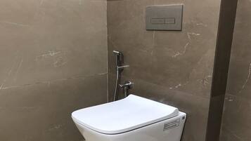 Un baño moderno con un inodoro blanco, ducha y panel de control en la pared.