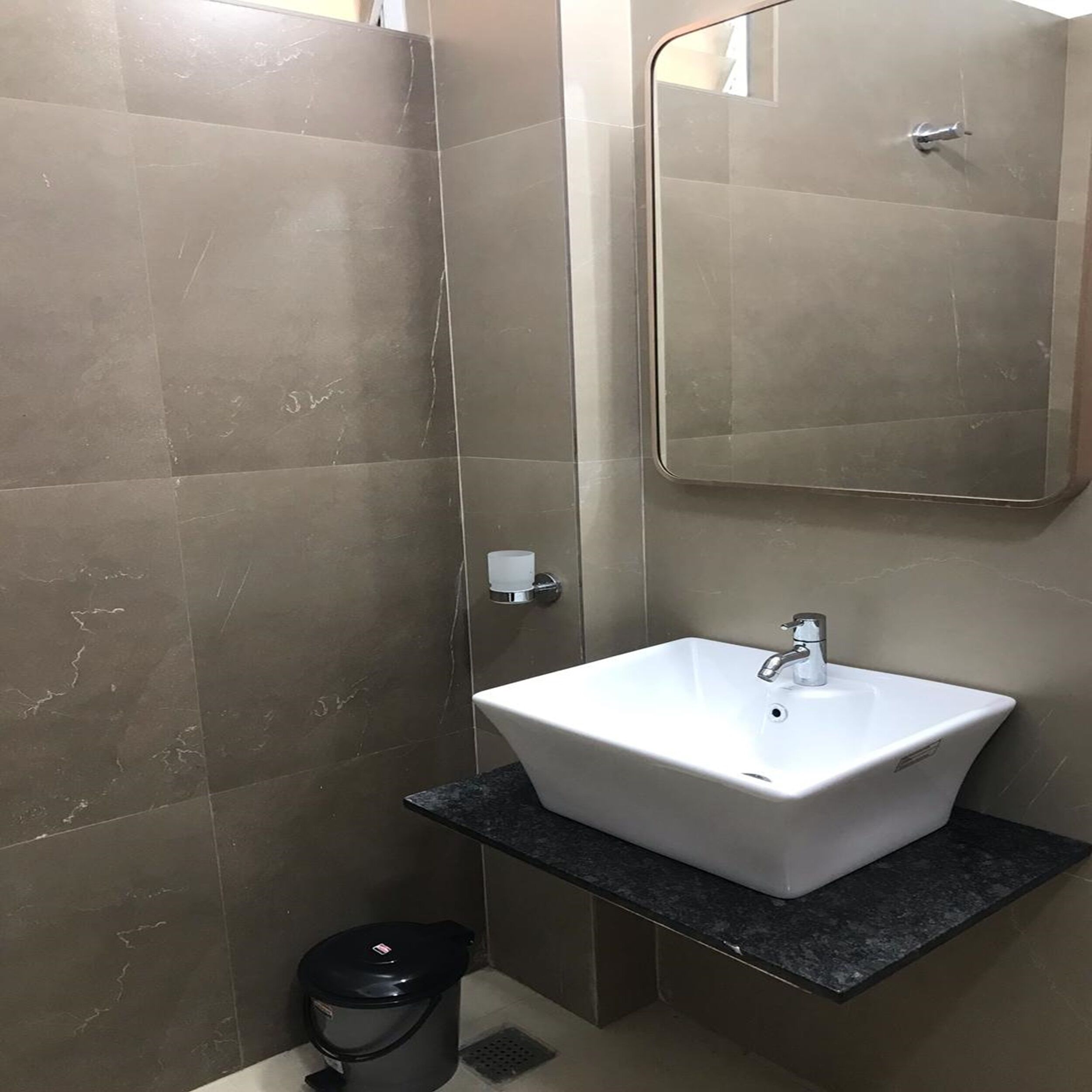 Een badkamer met een witte wastafel, een spiegel en een prullenbak.