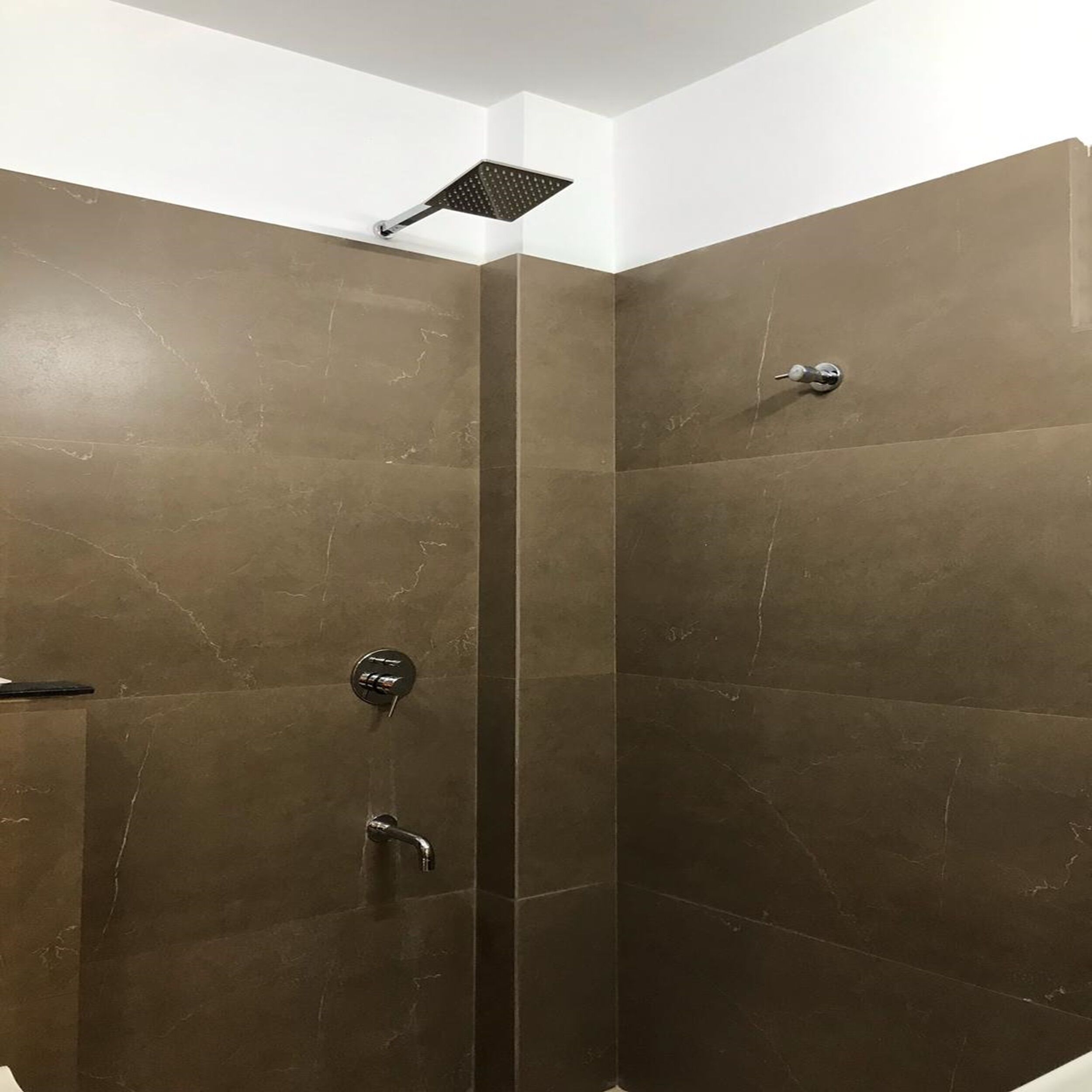 A shower with a square showerhead and a handheld shower attachment.