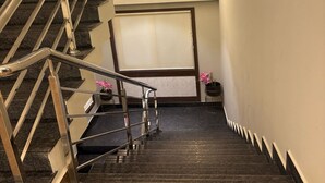 A modern staircase with metal railings and dark stone steps, leading to a landing with a large window and a small table with pink flowers. - EMBASSY PARK Near US consulate (Chennai)
