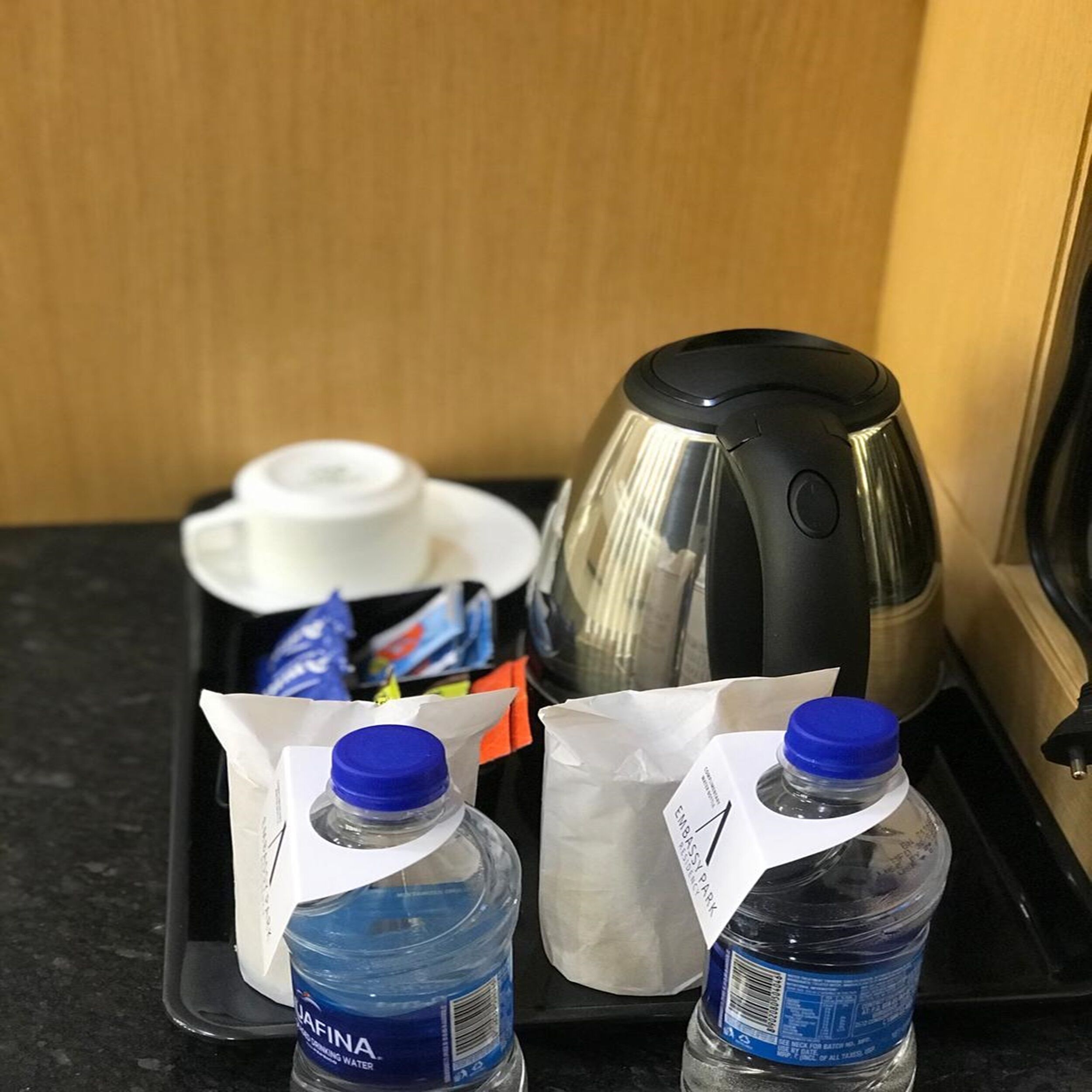 A kitchen counter with a coffee maker, two water bottles, a white cup, and a box of coffee pods.