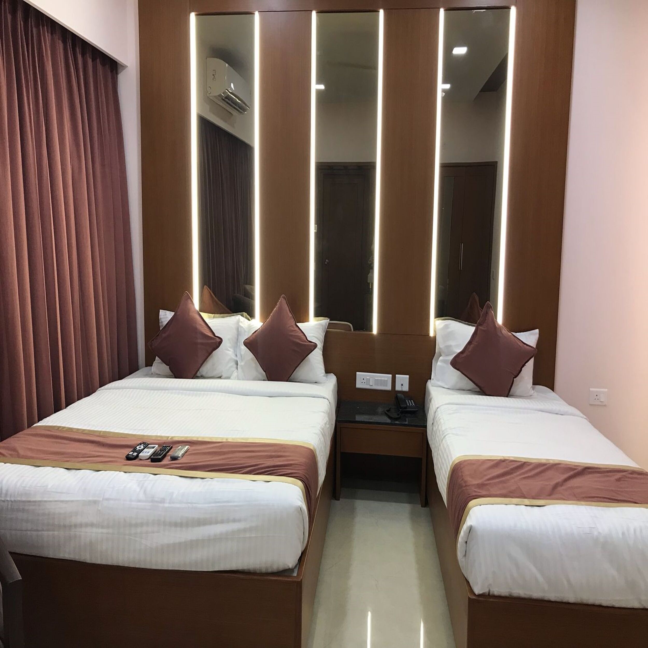 A hotel room with two beds, a mirror, and a bedside table with a phone.