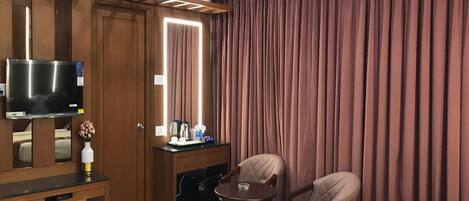Habitación de hotel con cama, escritorio con televisor, silla, mesita pequeña y unidad de aire acondicionado.