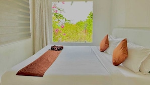 Ein ordentlich bezogenes Bett mit einer braunen Tagesdecke, weißen Kissen und Blick auf Grün hinter einem Fenster.