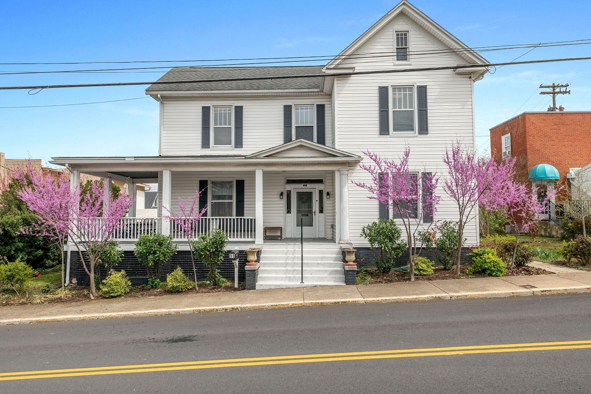 A two-story white house with a front porch, black shutters, and a brick garage.