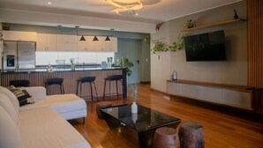 Una sala moderna con un sofá, una mesa de centro de vidrio y un televisor montado en la pared.