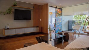 Una sala de estar moderna con un televisor de pantalla plana, piso de madera, una mesa de centro de vidrio y un ventanal con vistas al exterior.