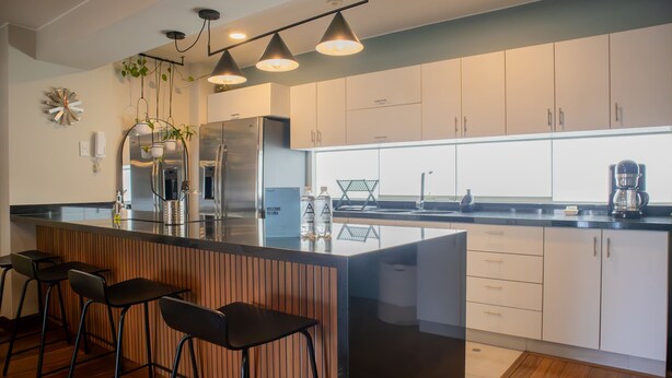 Una cocina moderna con una isla central, taburetes de bar, electrodomésticos de acero inoxidable e iluminación colgante.