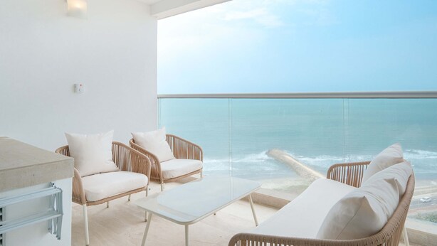 Een balkon met rieten meubels, een glazen tafel en uitzicht op de oceaan.