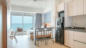 Een moderne hotelkamer met balkon, kitchenette, bed en bureau met stoelen.