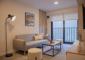 A modern living room with a sofa, ottoman, coffee table, floor lamp, and a painting on the wall.