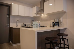 A modern kitchen with white cabinets, a coffee machine, and two stools.