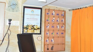 A hotel reception desk with a computer, a clock, a key rack, and a poster. - Hotel Tak (Udaipur)