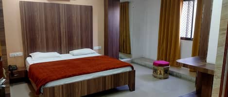 A modern hotel room with a wooden bed, an air conditioning unit, a small table, and a window with curtains.