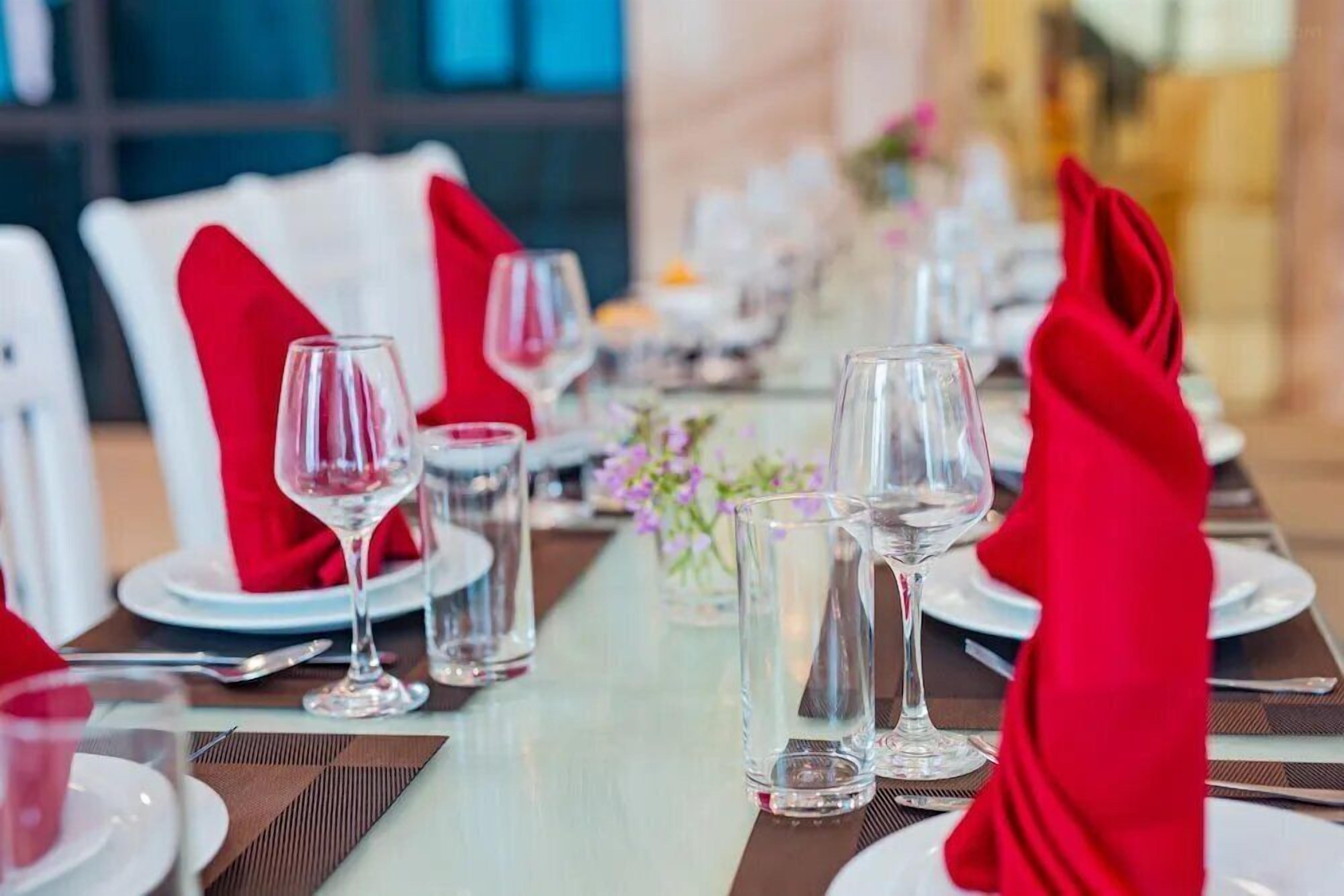 A dining table set with white plates, red napkins, and clear glasses.