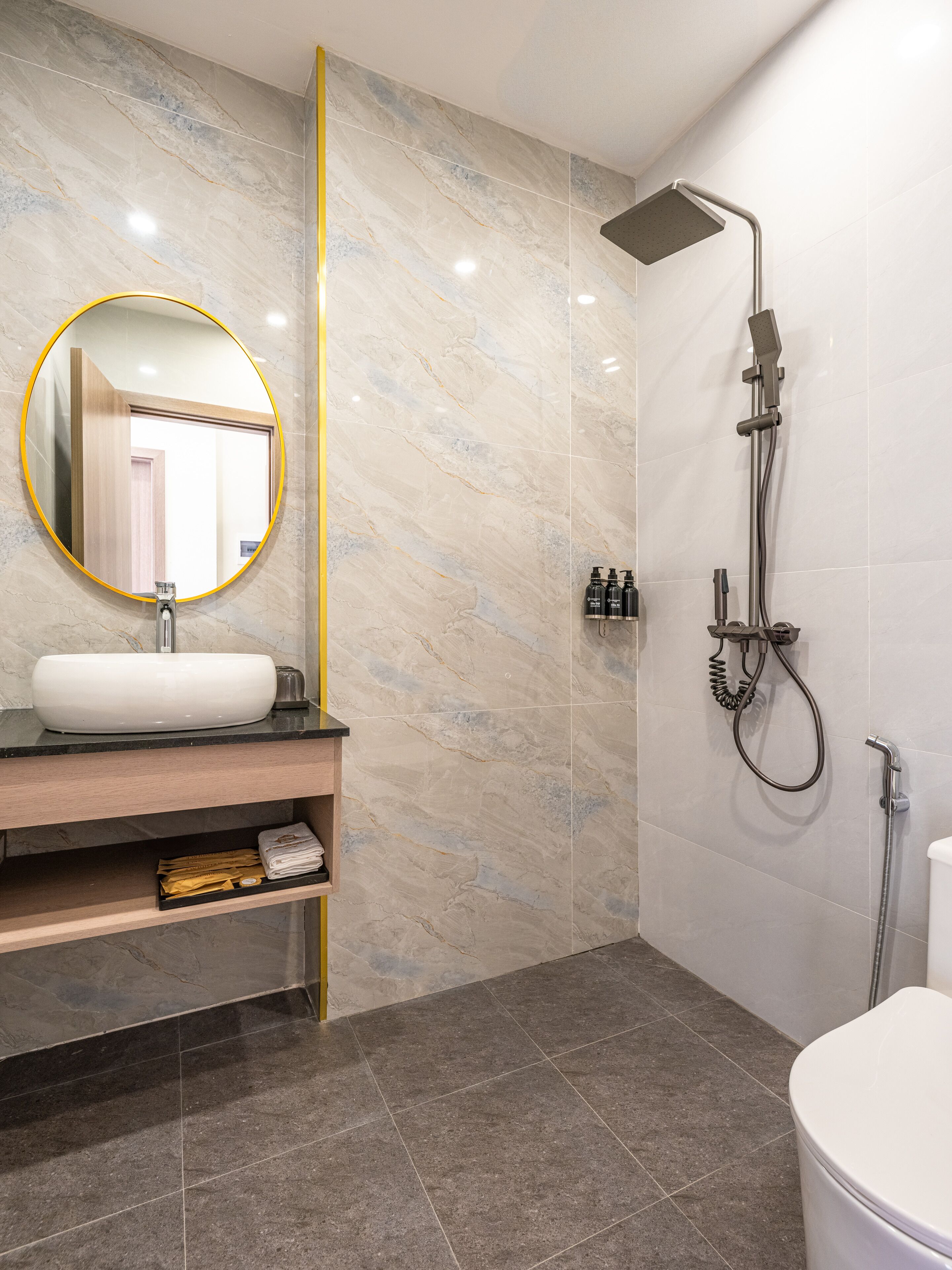 A modern bathroom with a marble vanity, a round mirror, a showerhead, and a toilet.